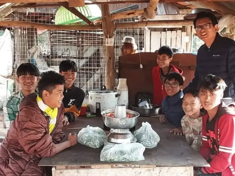 Jugendliche sitzen gemeinsam an einem Tisch unter einem Unterstand auf der Farm.