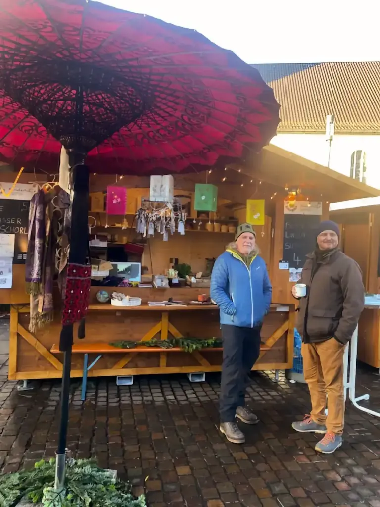 Zwei Vereinsmitglieder vor der geschmückten Hütte auf dem Weihnachtsmarkt Kressbronn.