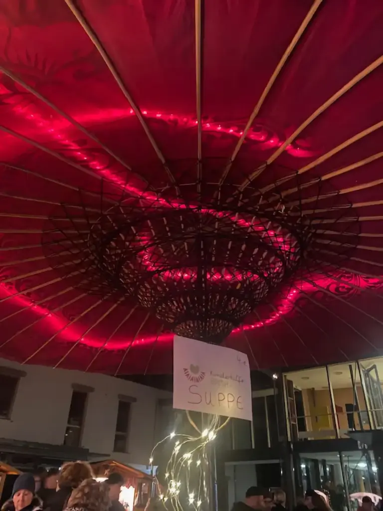Ein großer roter Schirm aus Burma mit Lichterkette über dem Stand.