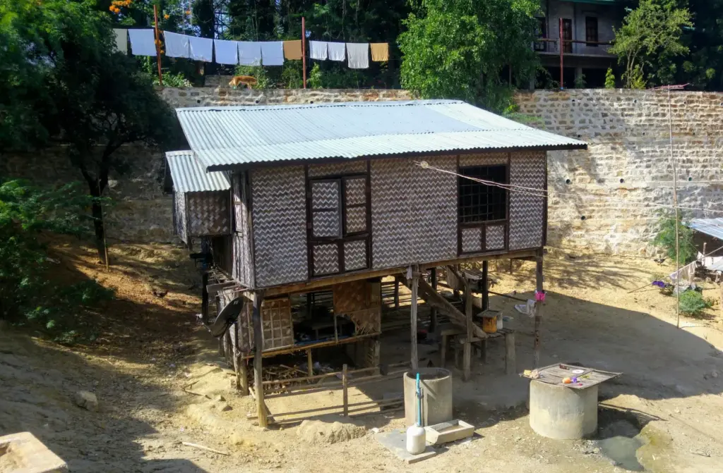Stelzenhaus aus Holz mit Wellblechdach, daneben ein Brunnen.