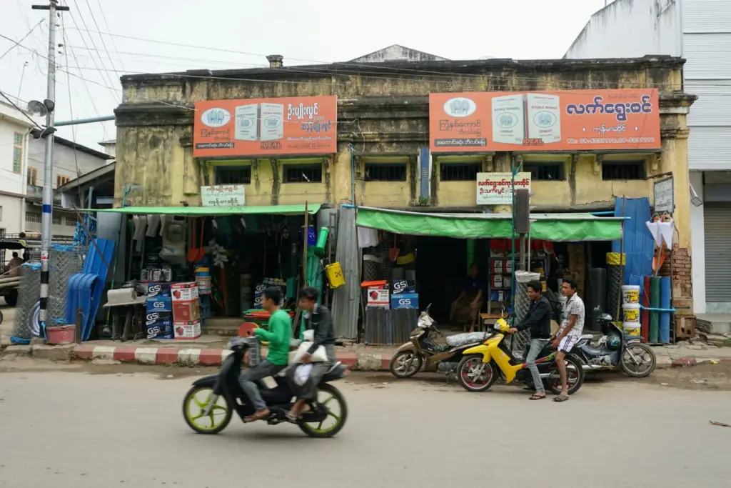 Straßenszene mit Mopeds vor Geschäften in einem Kolonialgebäude.