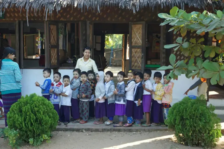 Schulkinder in Uniform stehen mit ihren Lehrern vor dem Schulgebäude.