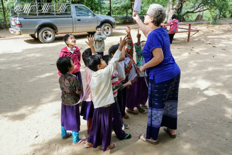 Eine Frau spielt mit einer Gruppe von Kindern im Freien ein Kreisspiel.