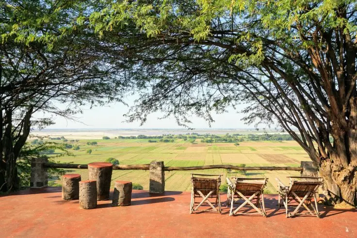 Terrasse des Lei Thar Gone Guesthouse mit Stühlen unter einem großen Baum und Blick auf die Ebene.