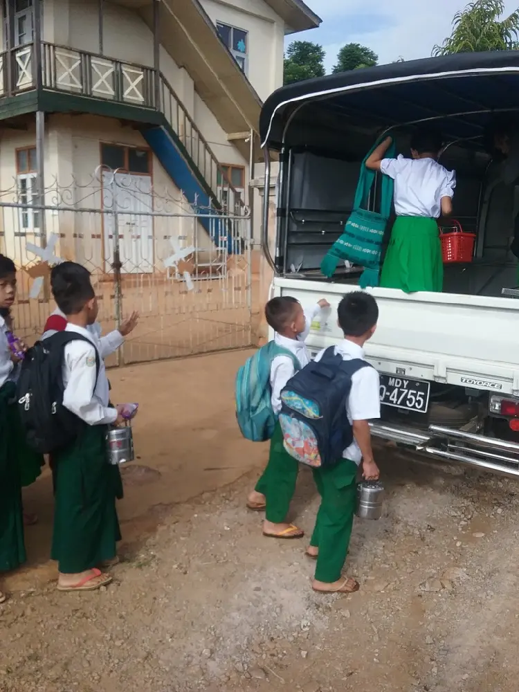 Schulkinder mit Rucksäcken steigen hinten in den Kleinlastwagen.