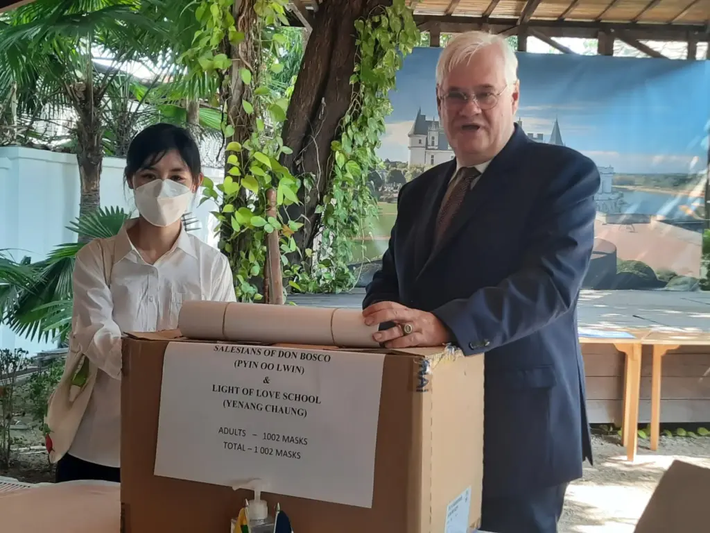 Übergabe der Maskenspende: Eine Frau und ein Diplomat stehen hinter einem Karton.