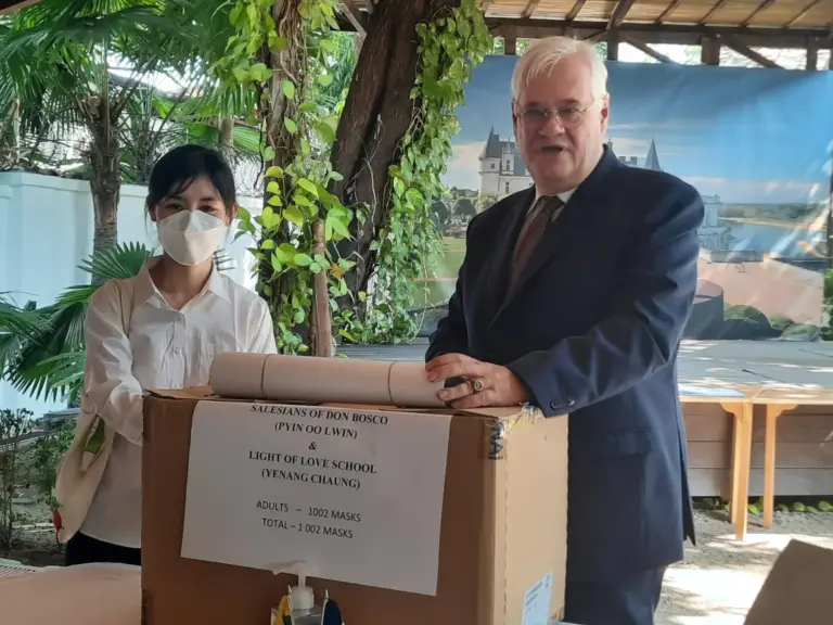 Übergabe der Maskenspende: Eine Frau und ein Diplomat stehen hinter einem Karton.