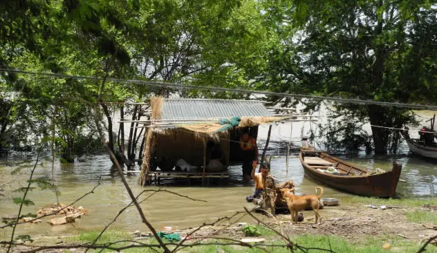 Überschwemmtes Ufer mit halb im Wasser stehender Hütte und einem Holzboot.