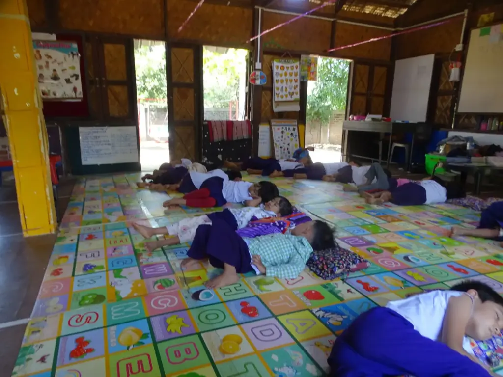 Kinder machen Mittagsruhe auf bunten Matten im Klassenraum.