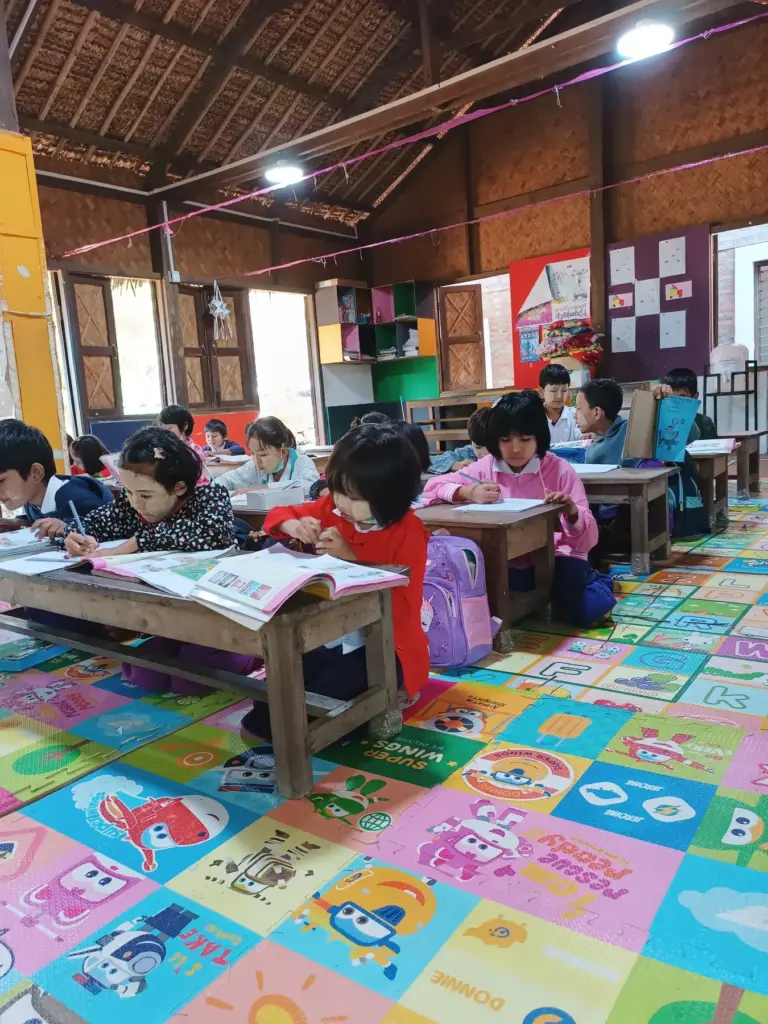 Kinder lernen an niedrigen Tischen auf bunten Bodenmatten im Klassenraum.