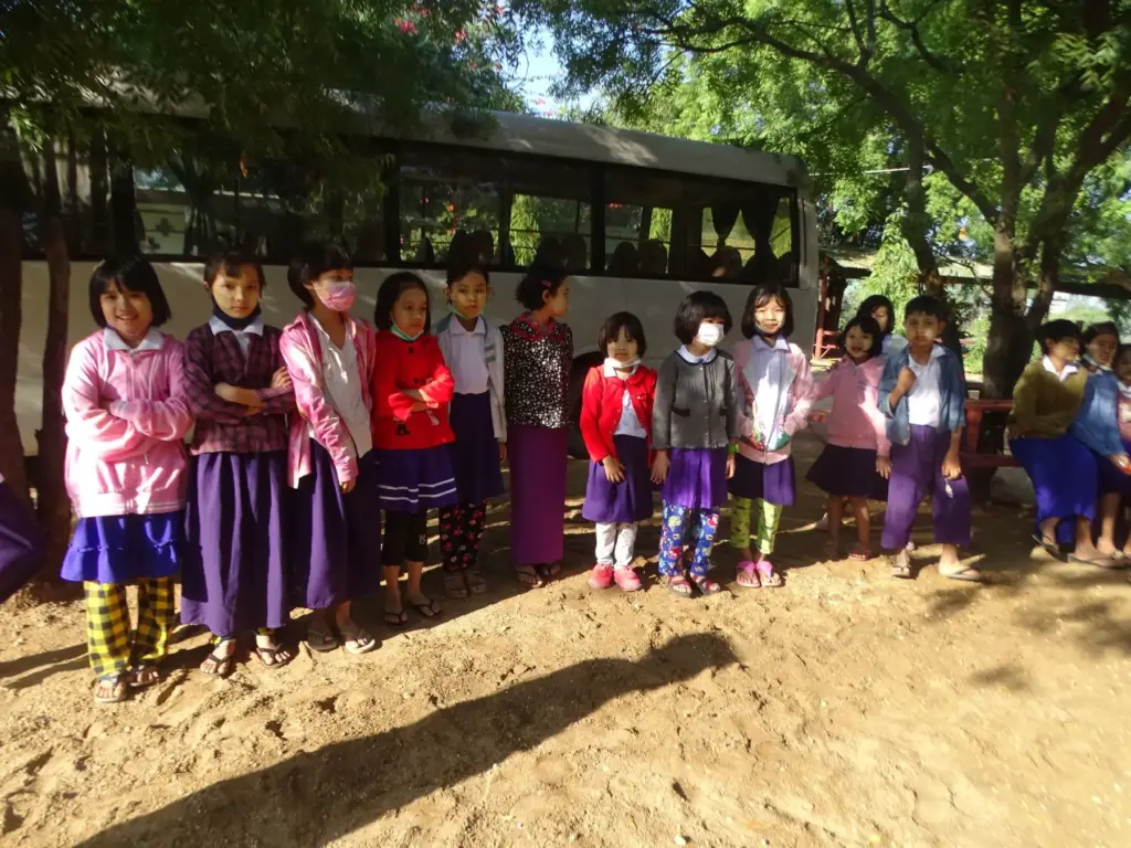 Kindergartenkinder stehen in einer Reihe vor dem Schulbus.