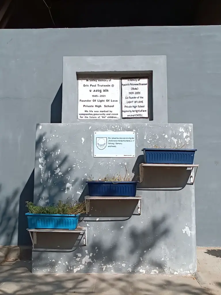 Gedenkstein mit Tafeln und Blumenkästen auf dem Schulgelände.