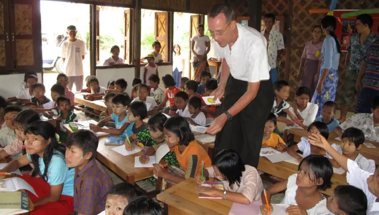 Schulklasse bei der Schuleröffnung im Juni 2009, Kinder an Tischen, Gäste stehen dahinter.