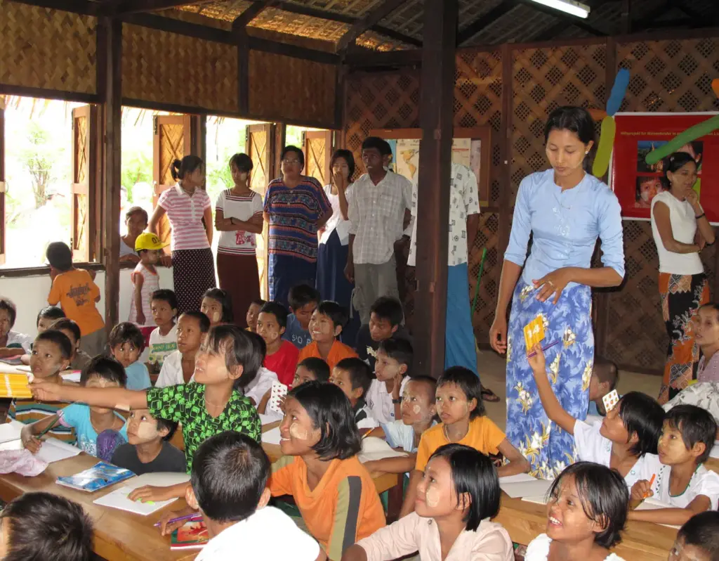 Voller Klassenraum mit Kindern an ihren Tischen und Gästen bei der Schuleröffnung 2009.