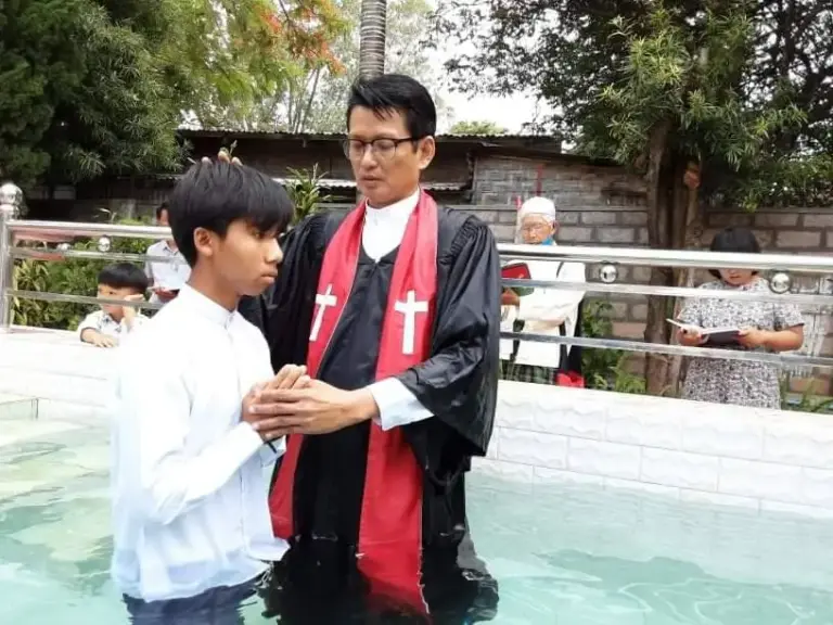 Ein Pastor im Talar tauft einen Jungen in einem Wasserbecken.