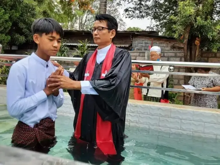 Ein Jugendlicher faltet bei der Taufe die Hände, neben ihm der Pastor.