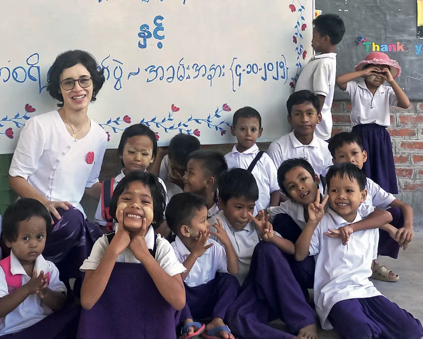 Zoe Trutwein, Leiterin der Light of Love School, sitzt lachend inmitten von Schulkindern in Uniform vor einer bemalten Wand.